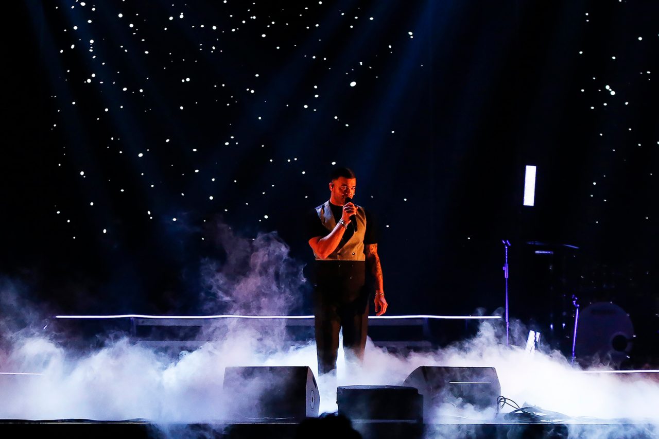Performer surrounded by low fog beneath a starry backdrop on the Ridin' With You tour.