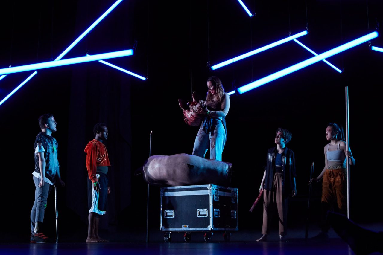 Angled blue light tubes above performers in Lord of the Flies.