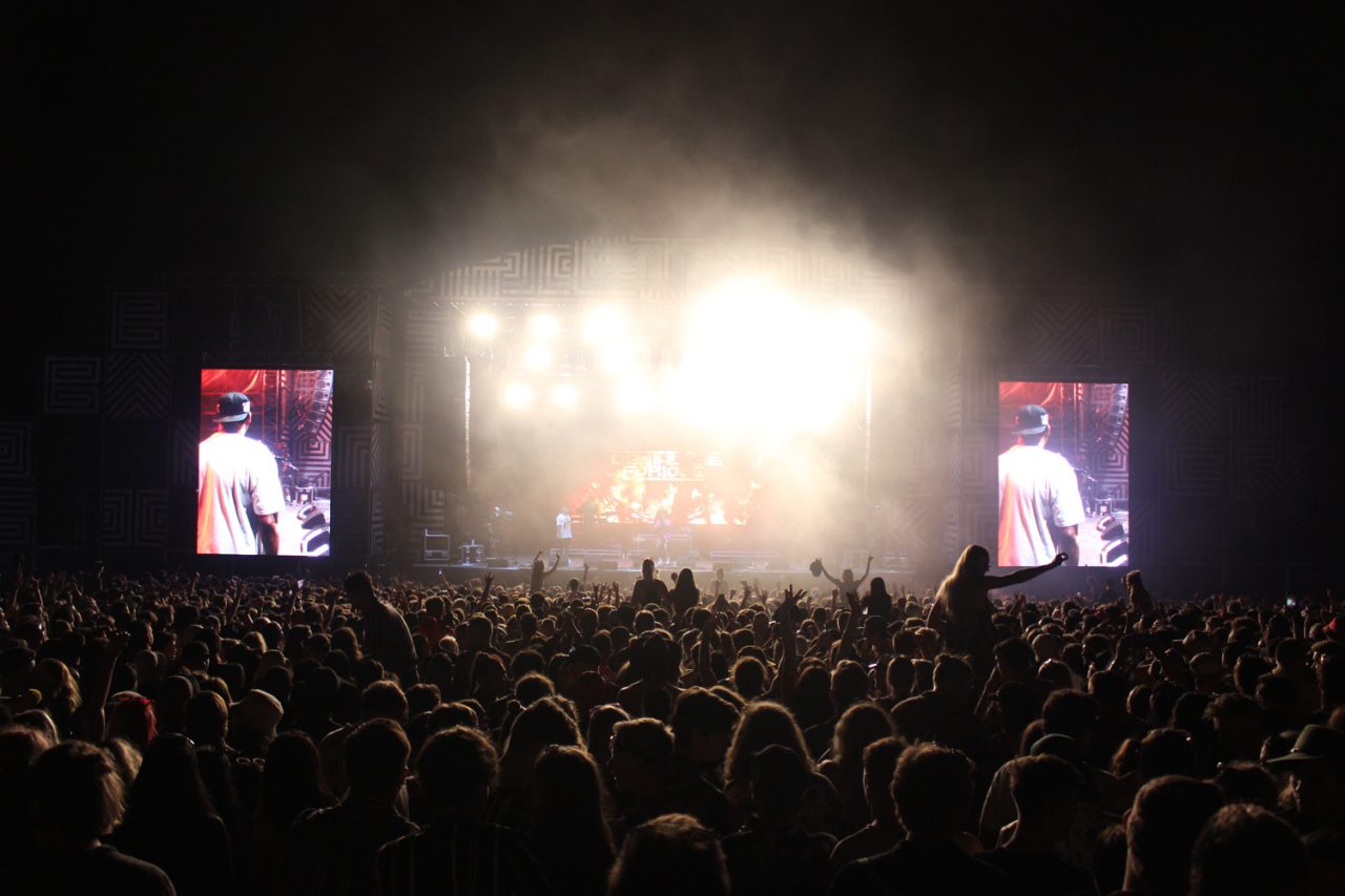 Bright stage lighting and two live video screens at Spilt Milk at night.