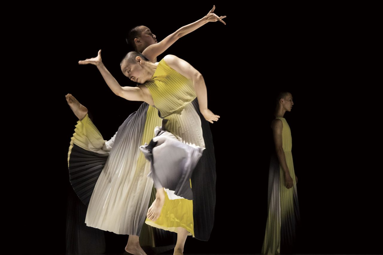 Two dancers with flowing pale costumes against a dark stage.