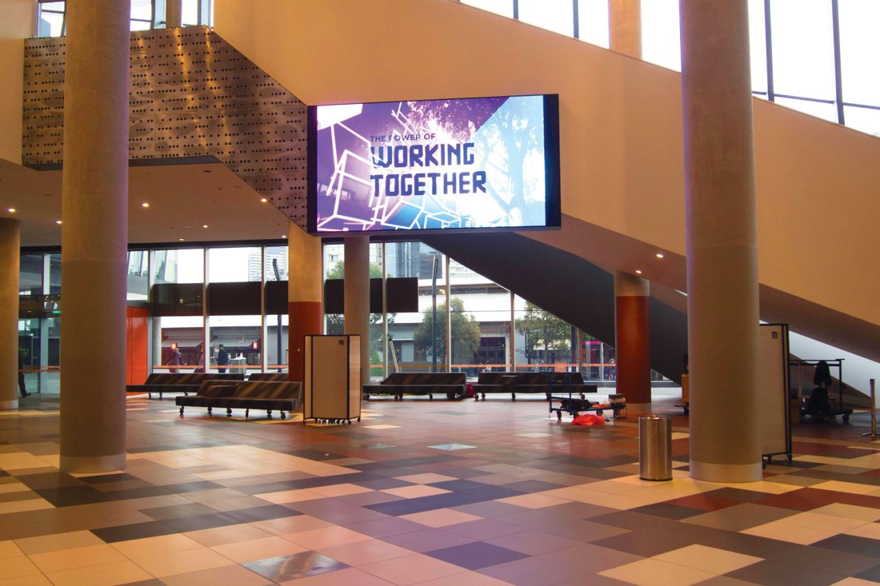 Working Together imagery on an indoor screen beside the MCEC stairs.
