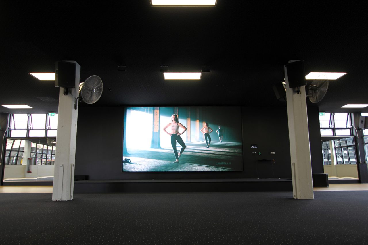Large video screen at the front of a Les Mills Auckland City fitness studio.