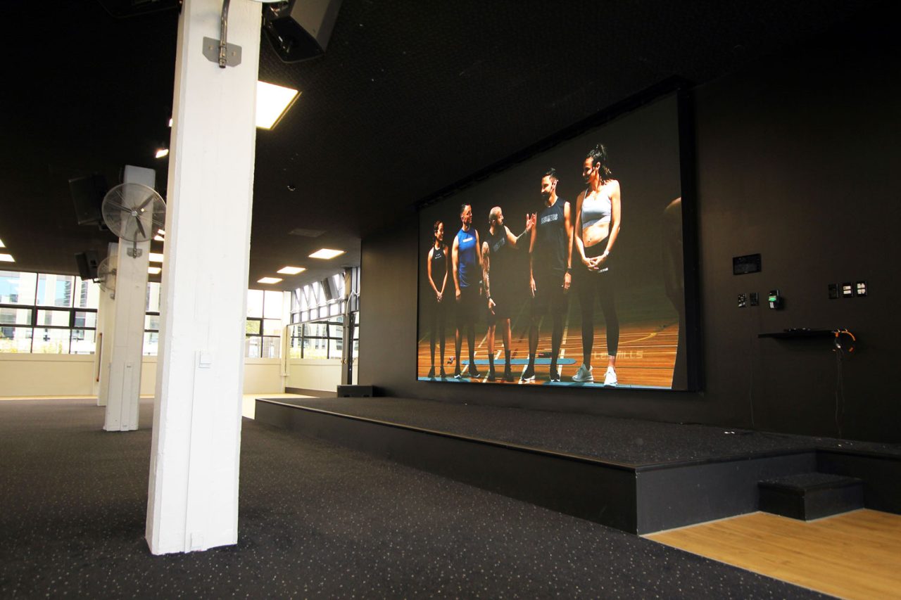 Group fitness footage on the large Les Mills Auckland City studio screen.