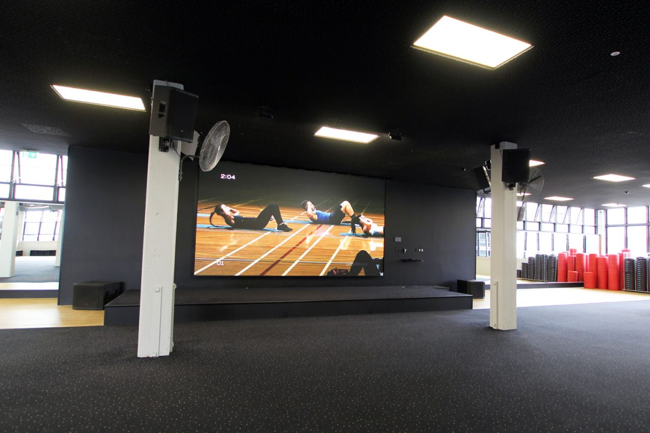 Wide view of the raised stage and video screen at Les Mills Auckland City.