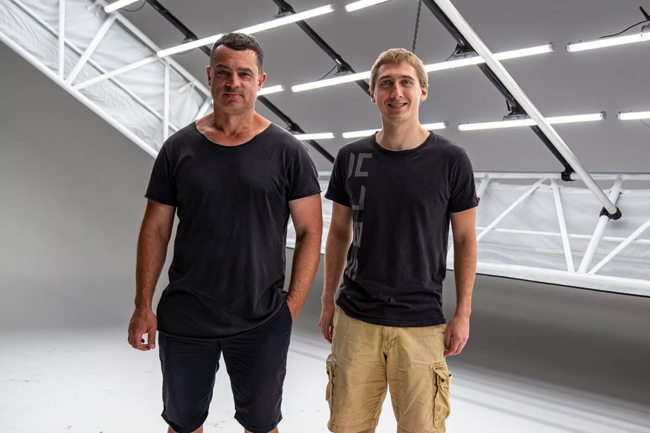 Two studio team members beneath the white tube-light grid at D1 Studios.