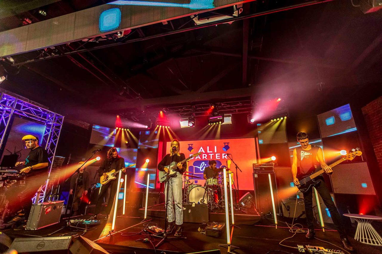 Musicians performing on the Delivered Live stage surrounded by upright LED tubes.