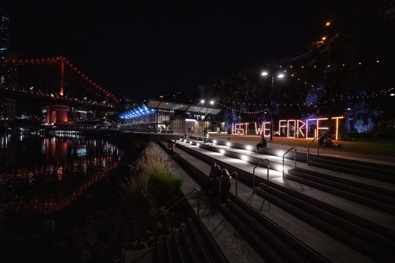 Lest We Forget light-tube sign beside the Brisbane River at night.