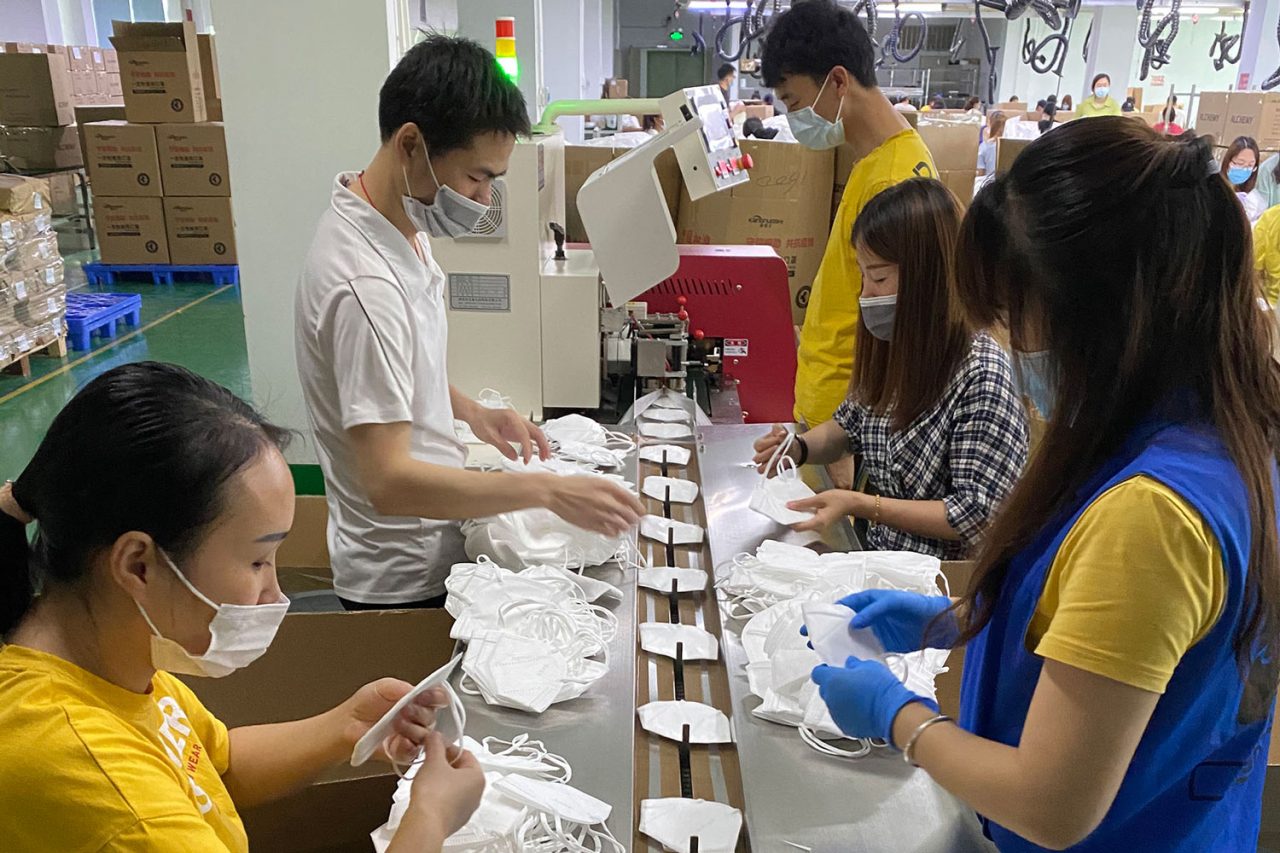 Workers checking and packing face masks at a production table.