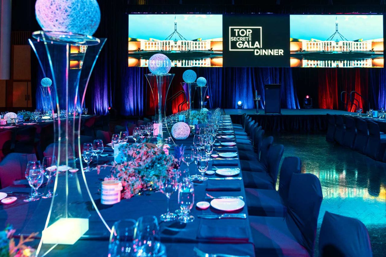 Set dining table beneath Top Secret Gala Dinner screens.
