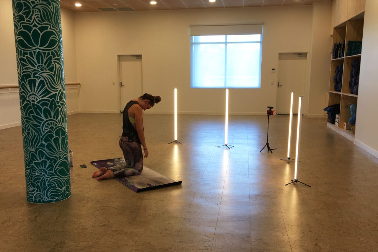 Instructor stretches on a mat between tube lights at Floating Lotus.