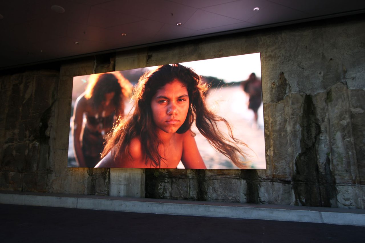 LED screen mounted against the stone wall at Barangaroo Reserve, showing a woman’s portrait.
