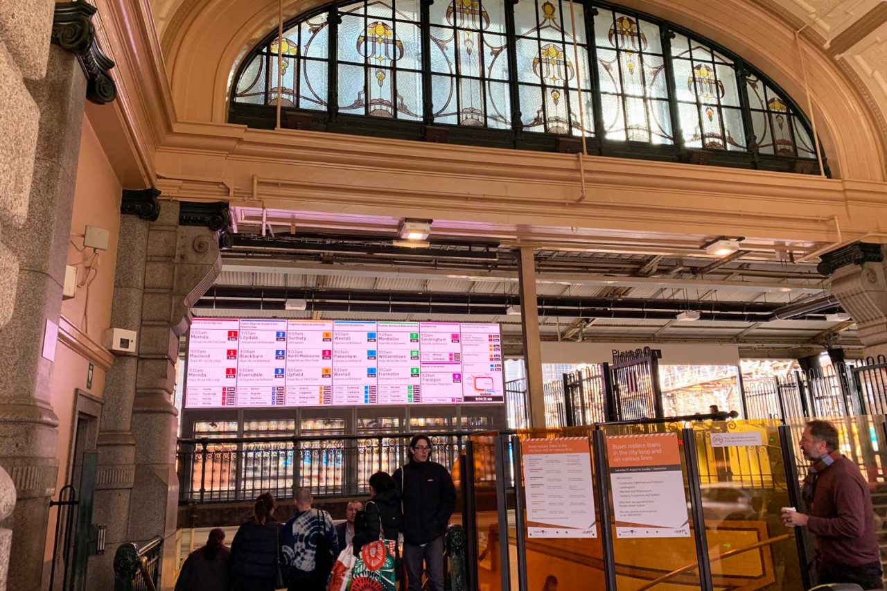 Electronic departure board beneath the large arched window at Flinders Street Station.