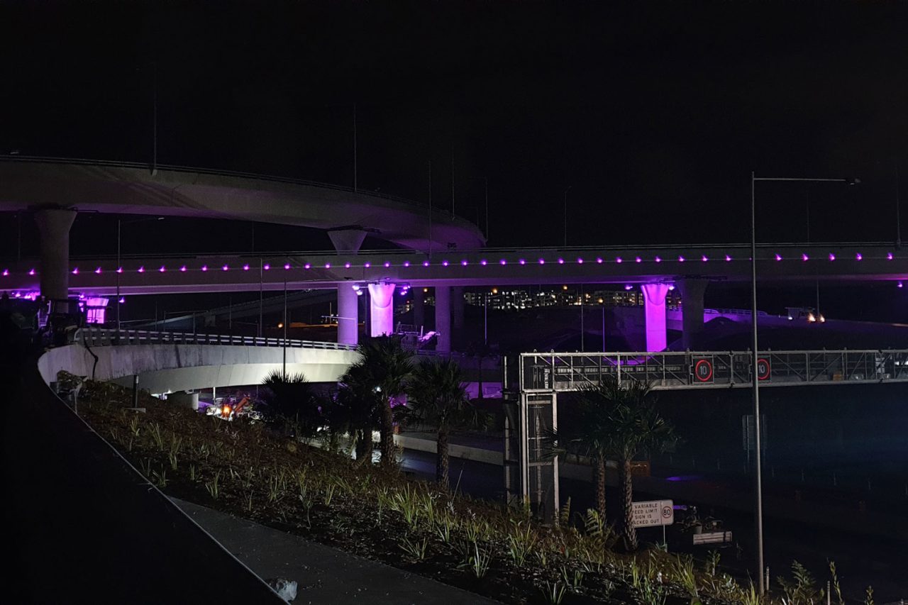 Purple architectural lighting around the WestConnex M8 motorway infrastructure at night.