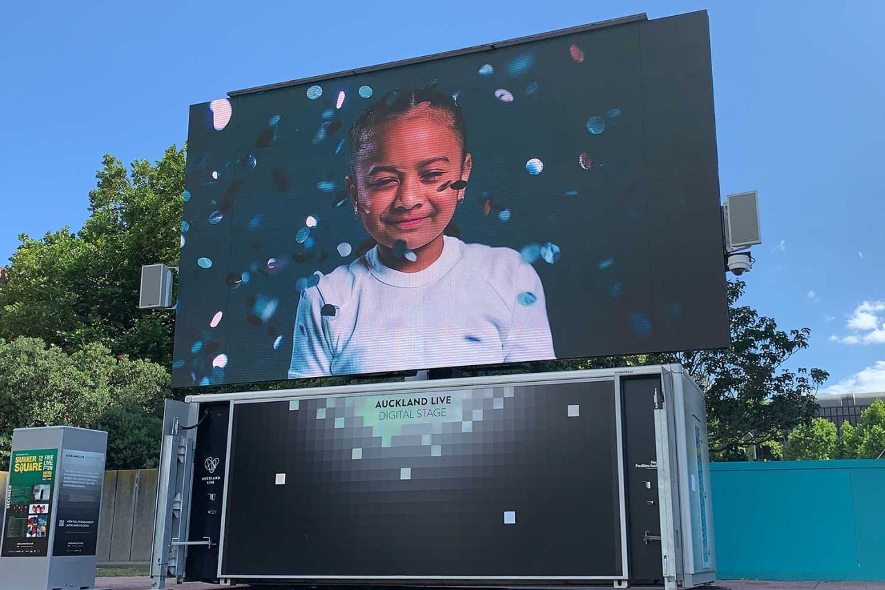 A smiling child in video footage on the Auckland Live outdoor screen.