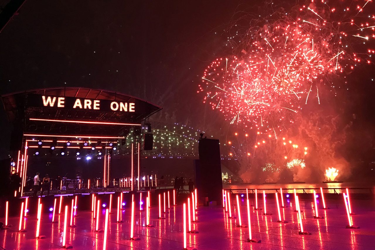 Red fireworks above the We Are One stage and rows of illuminated light tubes.