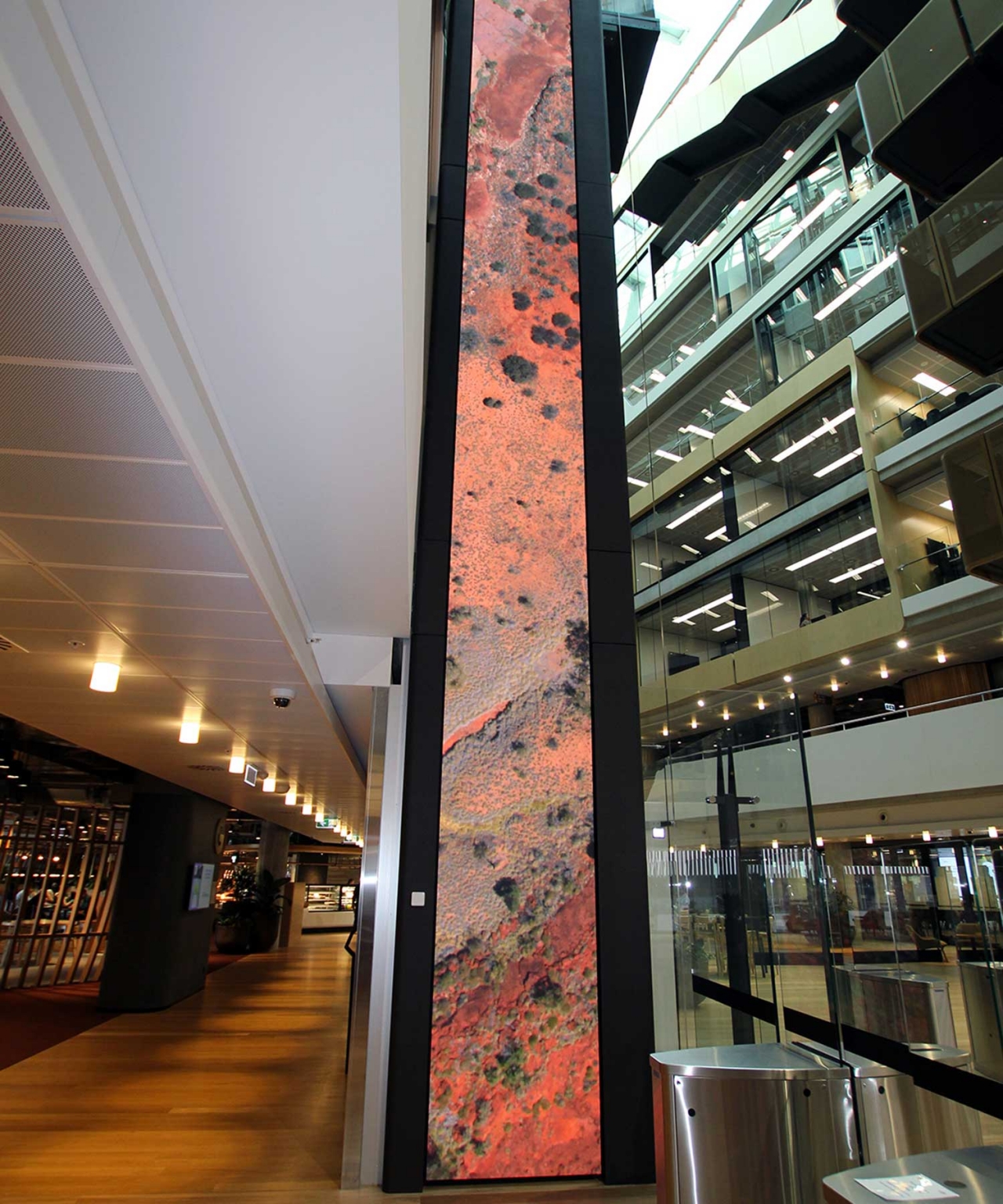 Digital LED column showing warm-coloured imagery beside the glass lift shaft.
