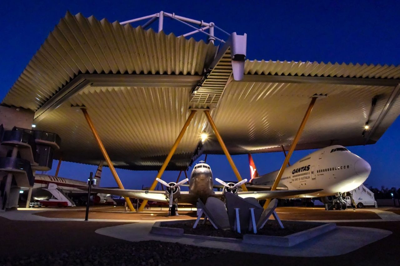 Evening view of aircraft beneath the large illuminated Qantas Founders Museum canopy.