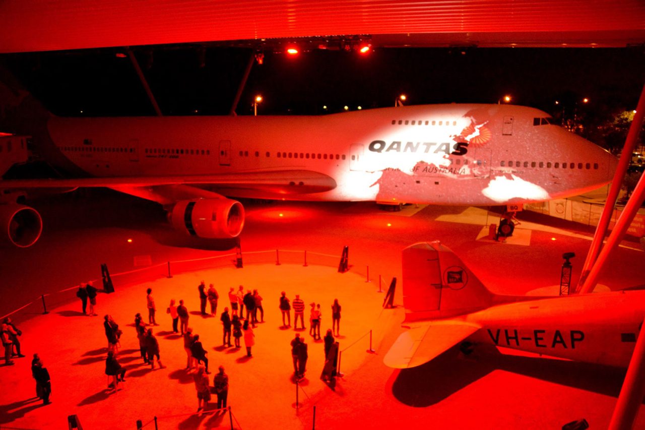 Visitors beneath an aircraft lit red during a projection show at Qantas Founders Museum.
