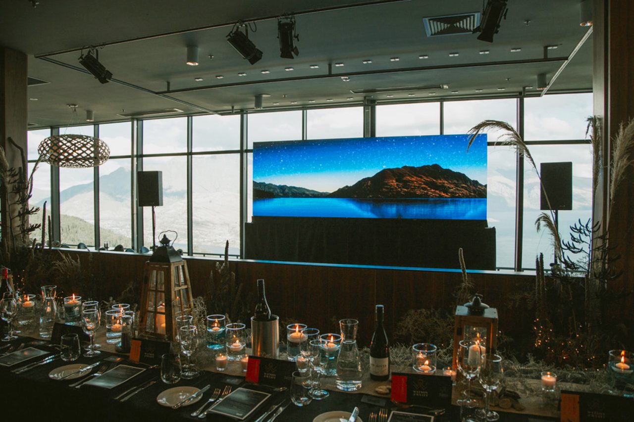 Landscape imagery on the screen above banquet tables at a Queenstown event.
