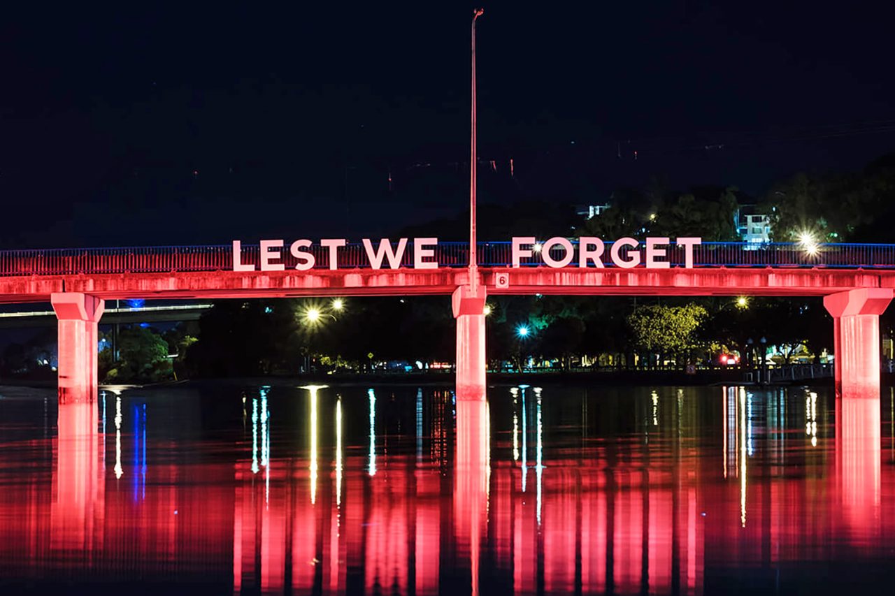 Lest We Forget lettering above red-lit columns reflected in the water at Currumbin.