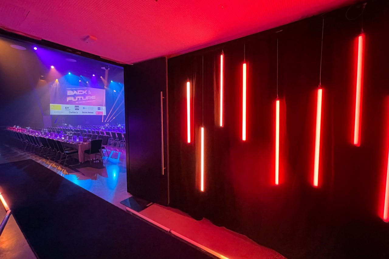 Red tube lights along a wall beside the Property Council gala event screen.