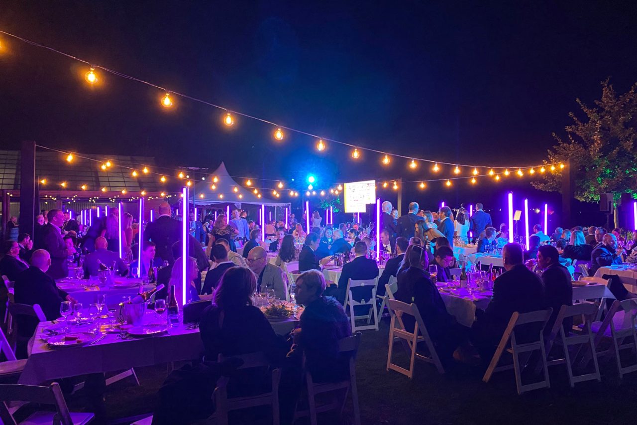 Guests beneath string lights and purple tube lighting at the outdoor AHA Awards dinner.