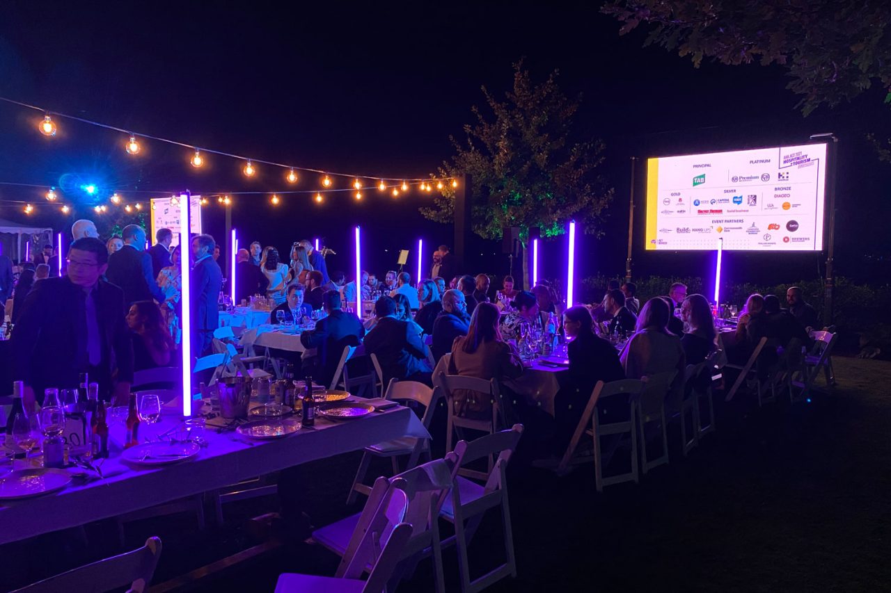 The AHA Awards outdoor banquet in Canberra lit purple and blue, with an event screen beside the tables.