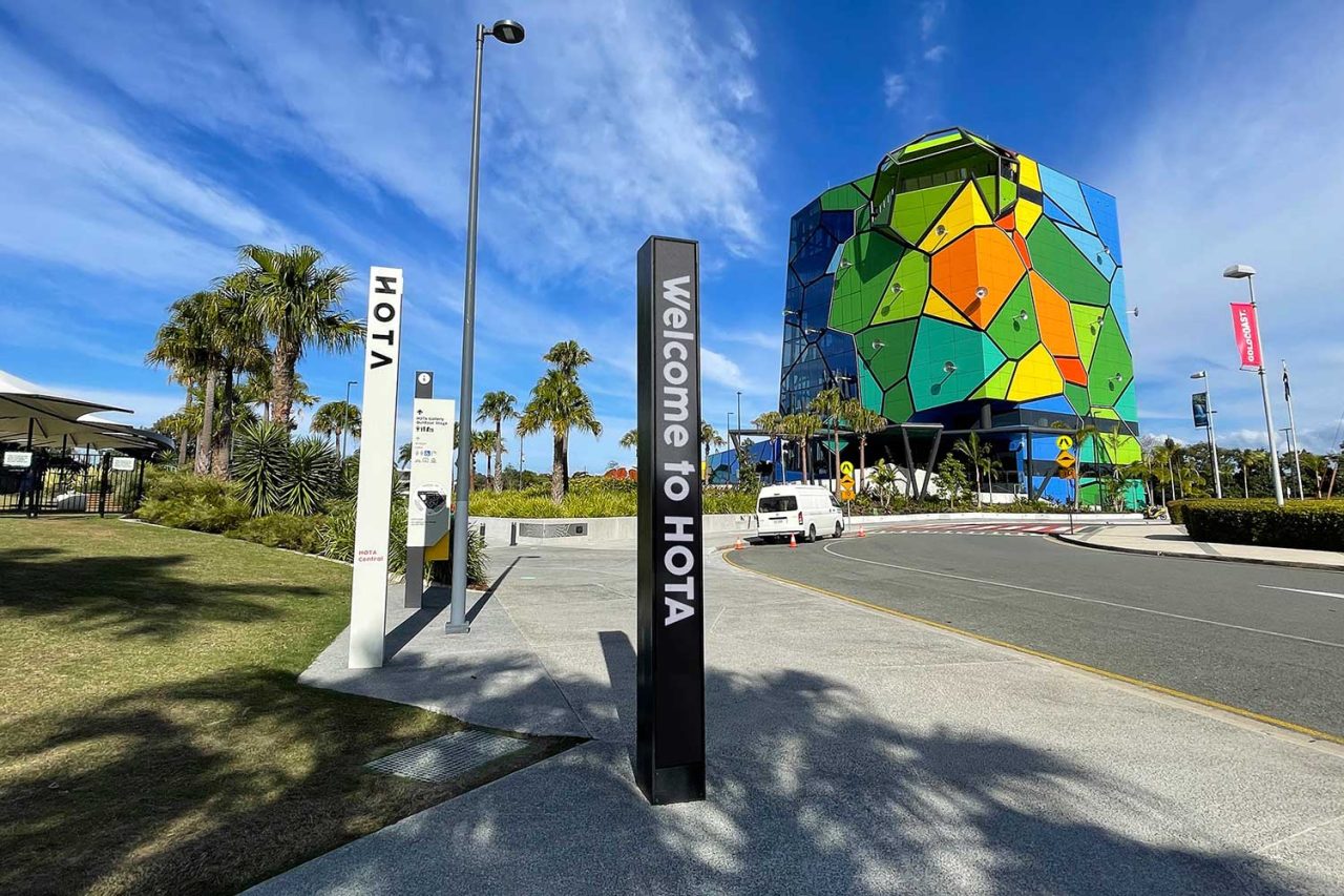 Tall vertical HOTA Gallery signs in front of the precinct's green angular building.