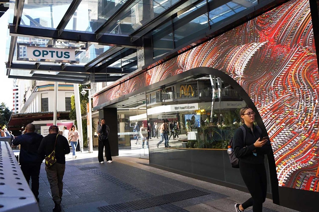 Orange and red imagery wraps around the curved digital display above the Optus store entrance.