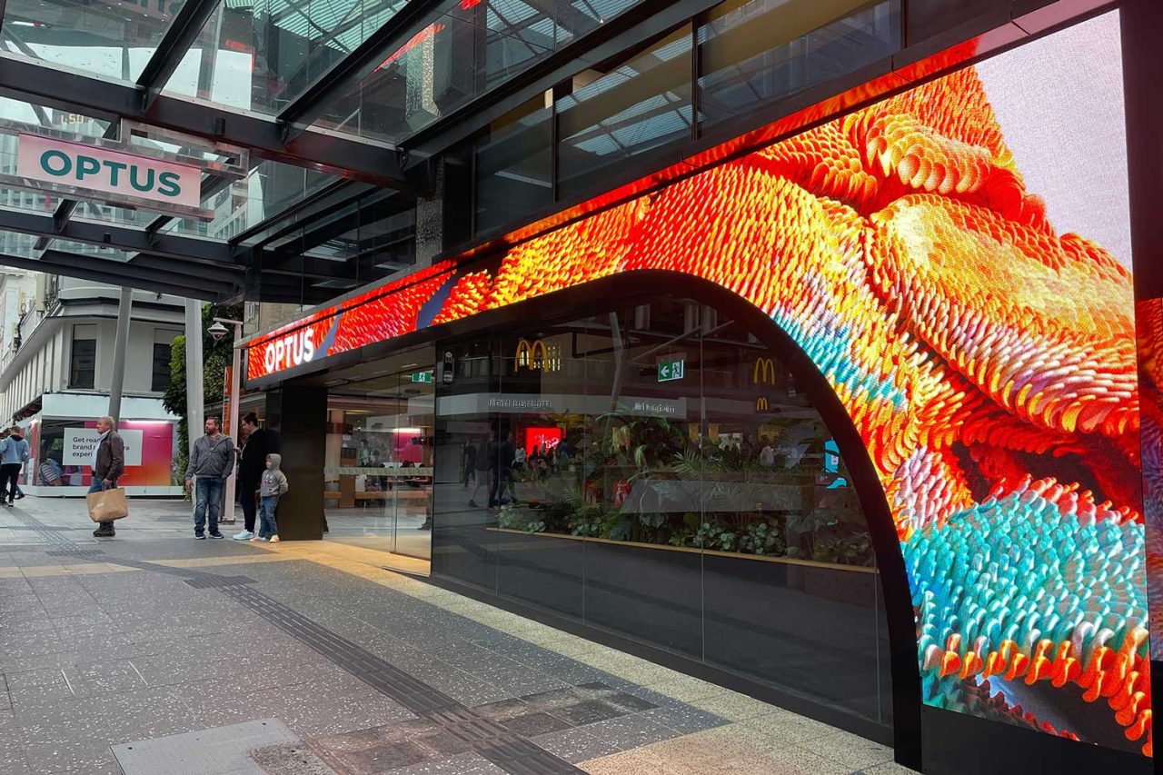 Yellow and teal patterns on the curved digital display around the Optus store entrance.