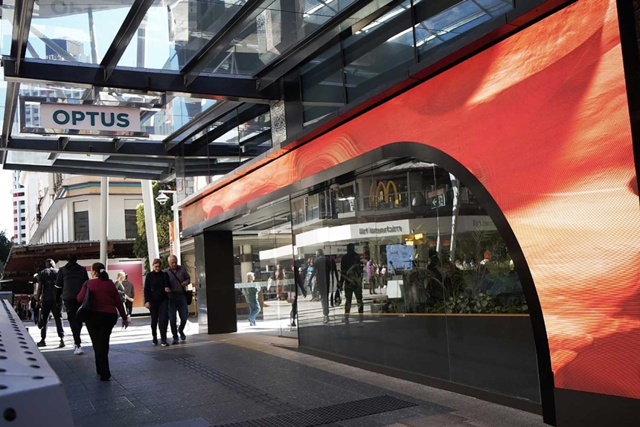 Warm red imagery across the digital facade of the Optus store.