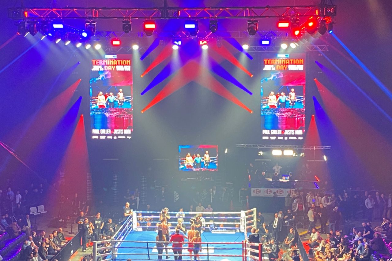 Boxing ring beneath coloured beams and large screens at the Gallen versus Huni event.