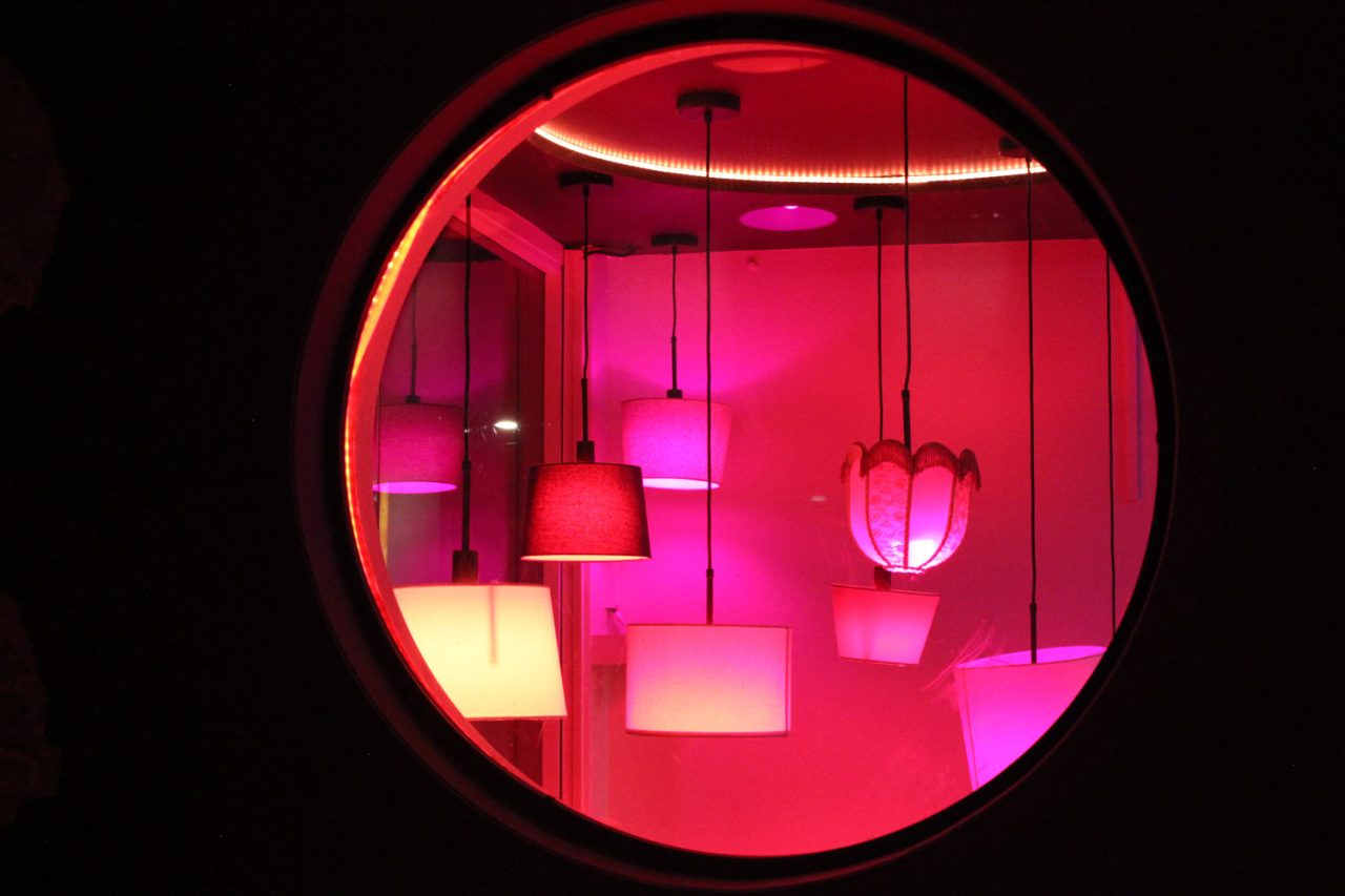 Pendant bulbs glow pink through a circular window at One22 bar.