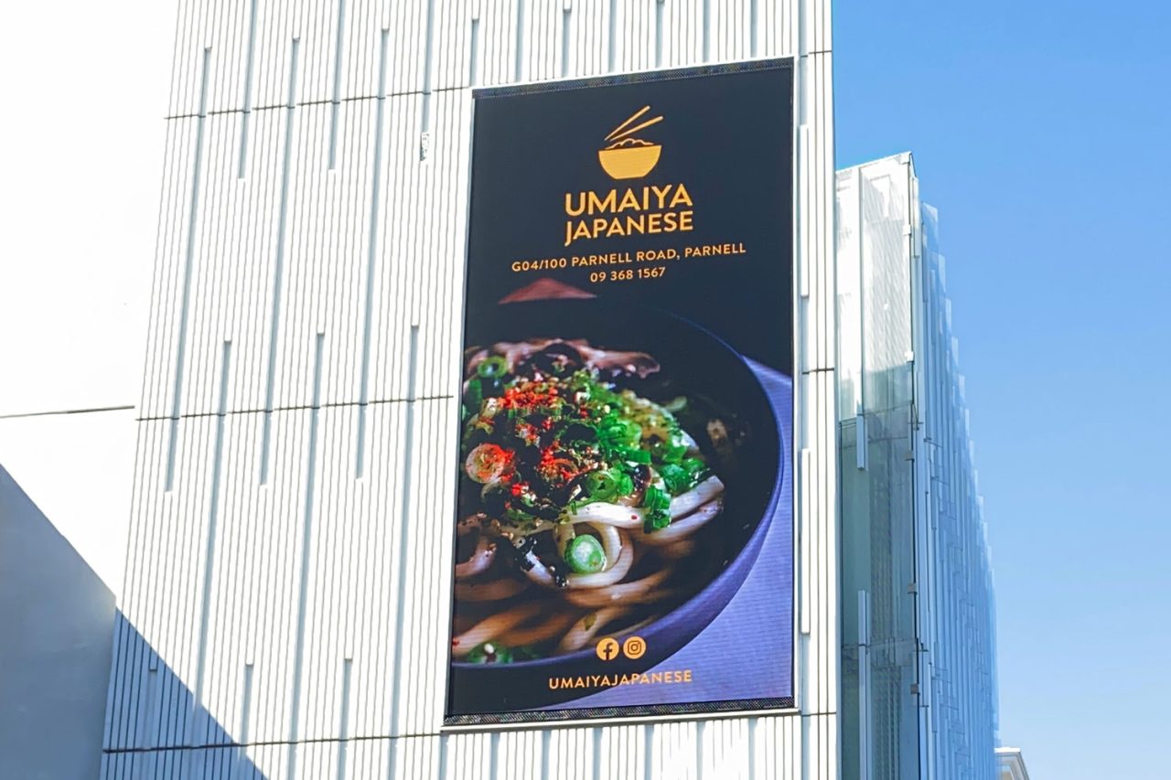 Vertical LED screen showing a food advertisement on the facade at 100 Parnell Road, Auckland.