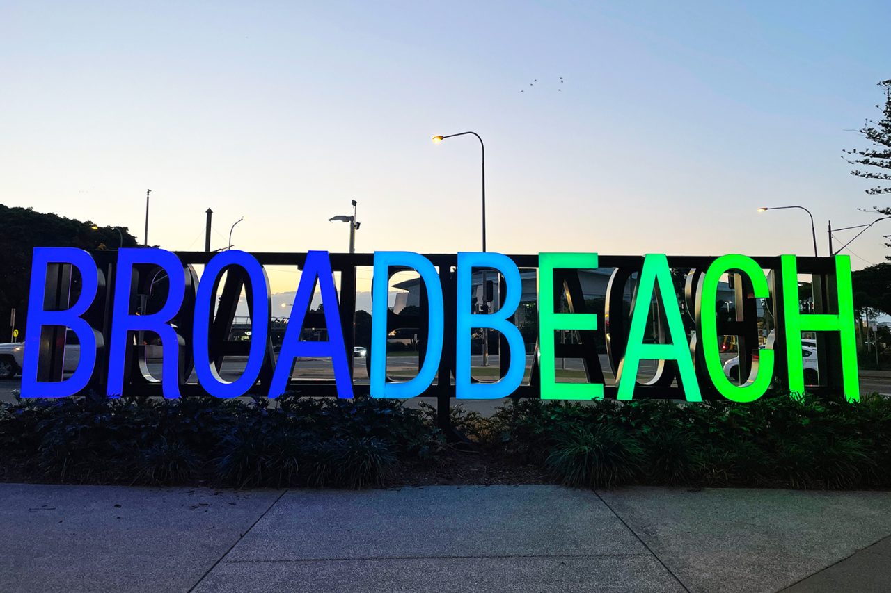 The Broadbeach sign lit blue and green against the evening sky.