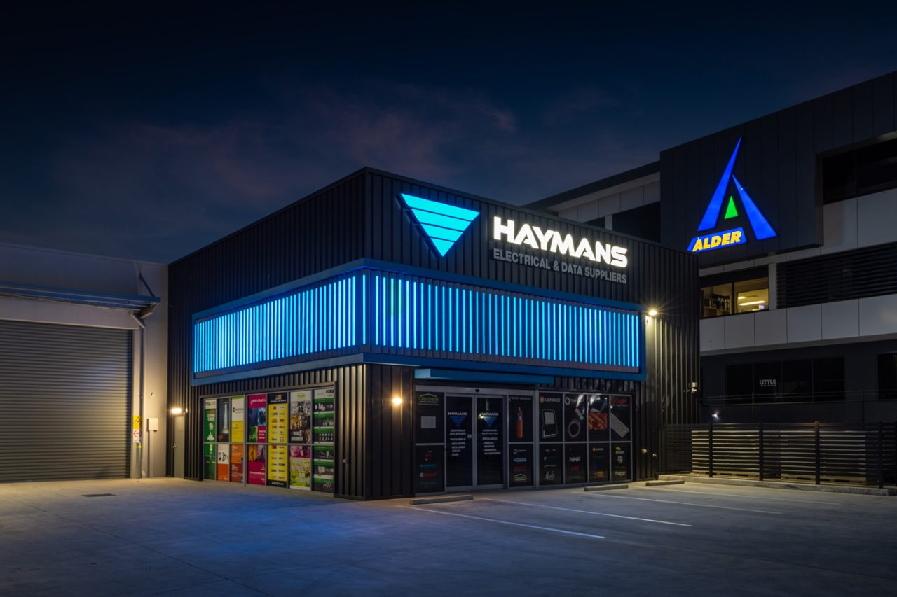 Blue vertical graphics wrap around the Haymans Electrical store facade at night.