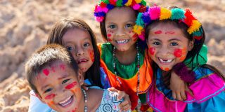 Children smiling together in colourful costumes, flower garlands and face paint.