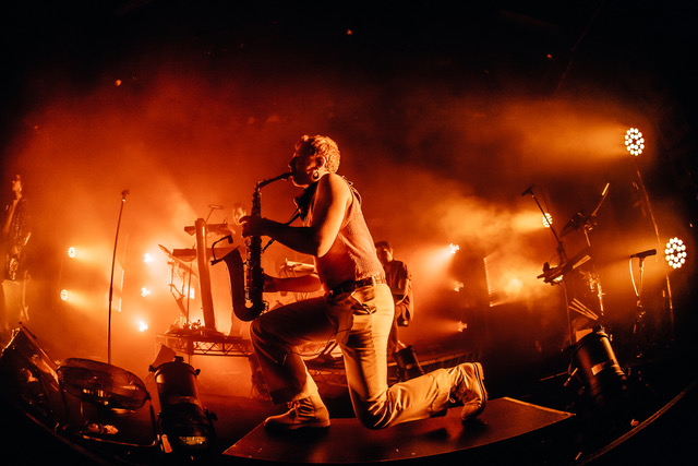 Performer kneels on stage amid orange lighting at the Client Liaison show.