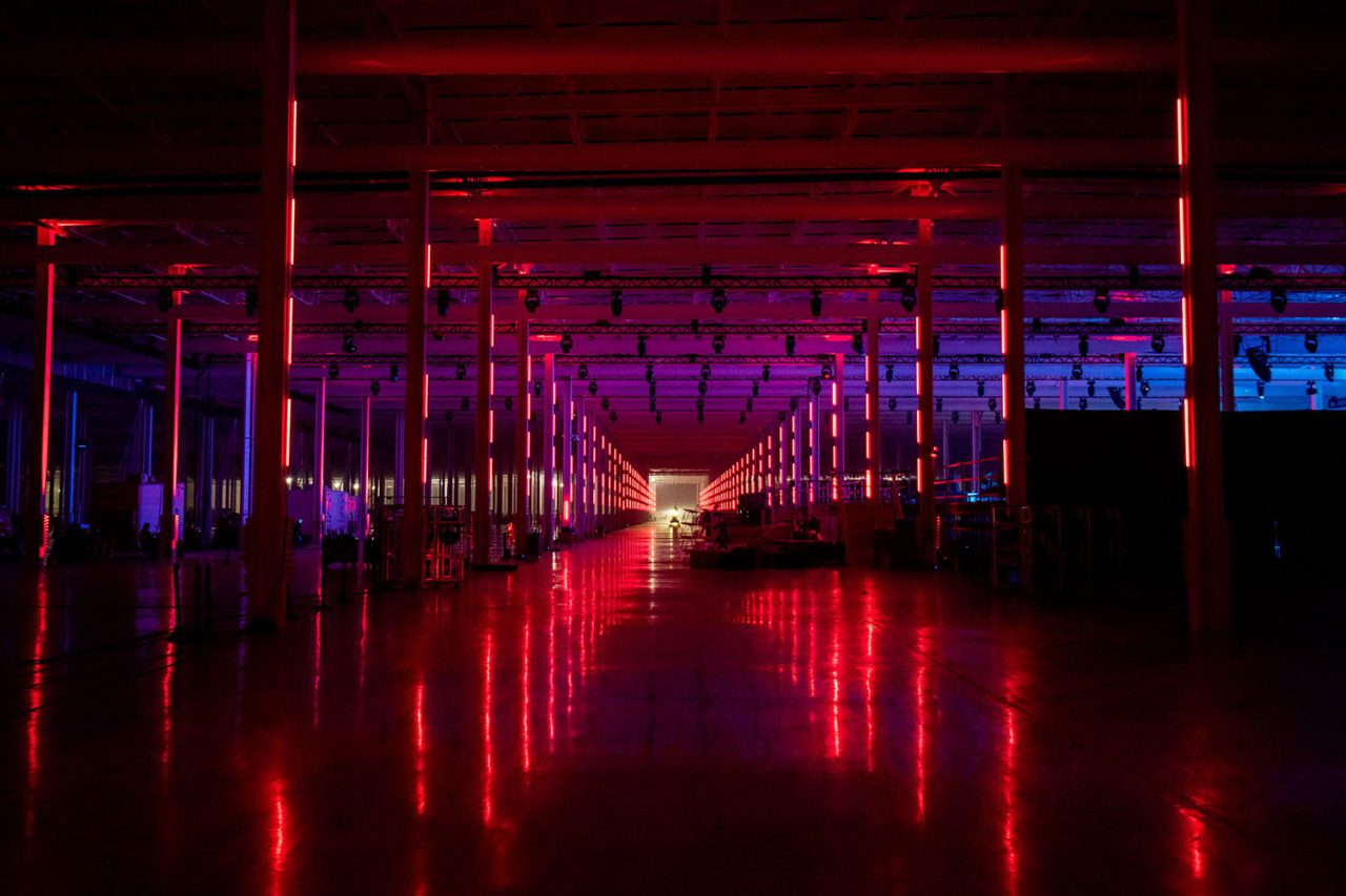 Red light tubes reflected along an aisle at Tesla's Cyber Rodeo.