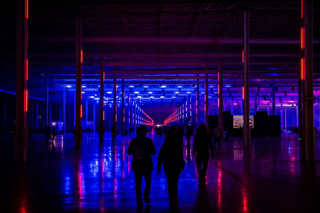 Visitors walk through a blue-lit factory aisle at Tesla's Cyber Rodeo.