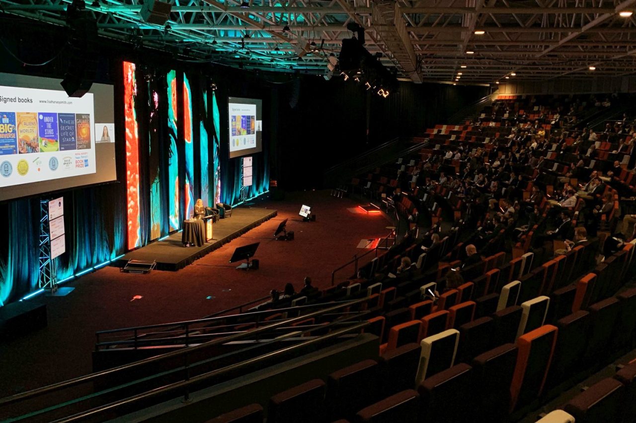 Side view of the audience and illuminated video columns at the Locate22 conference.