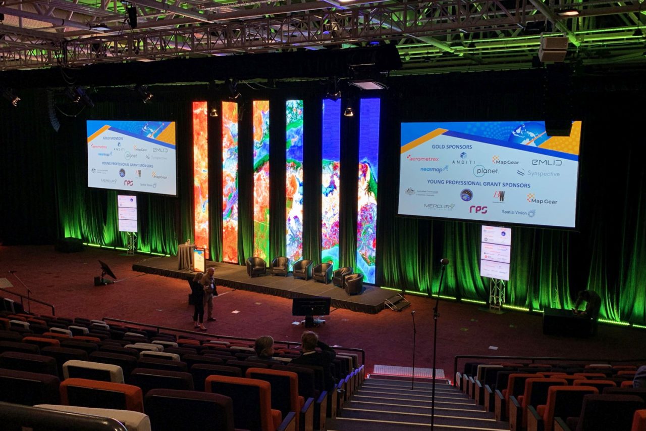Green uplighting beneath the video columns and presentation screens at Locate22.