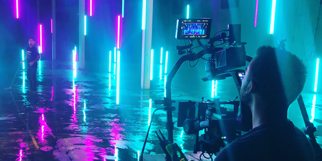 Camera operator filming among cyan and magenta light tubes.