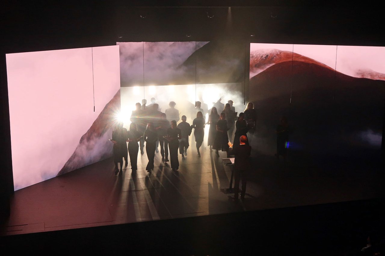 Performers silhouetted by bright backlighting between the Taumata stage screens.