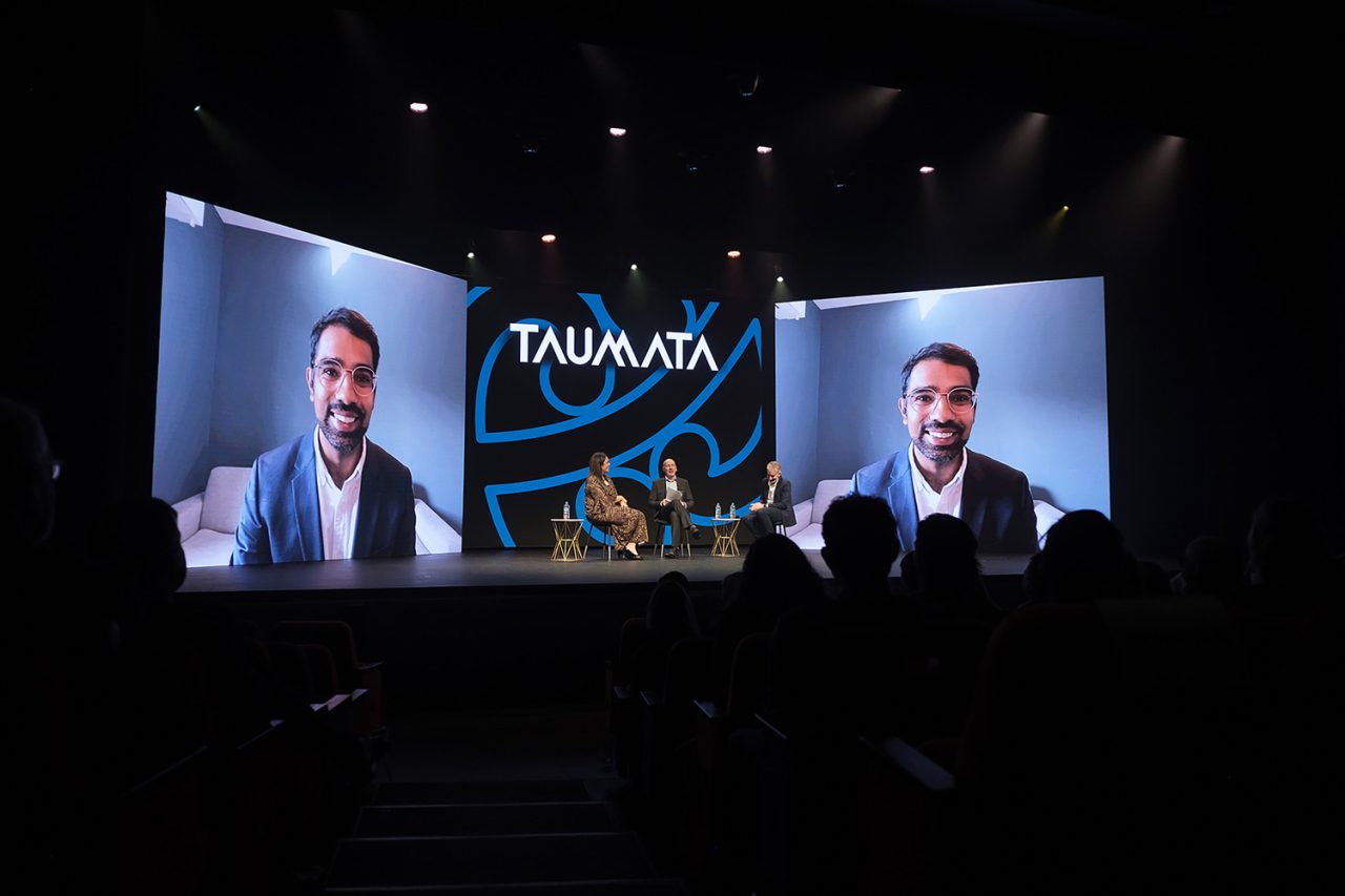 A remote speaker appears on the large Taumata 2022 screens above seated stage guests.
