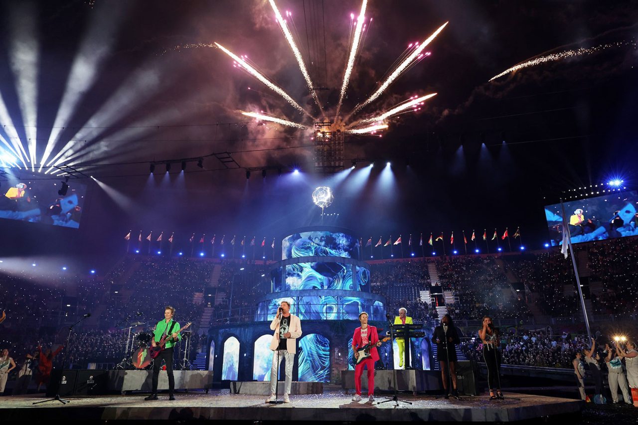 Performers beneath fireworks and stage beams at the Birmingham 2022 ceremony.