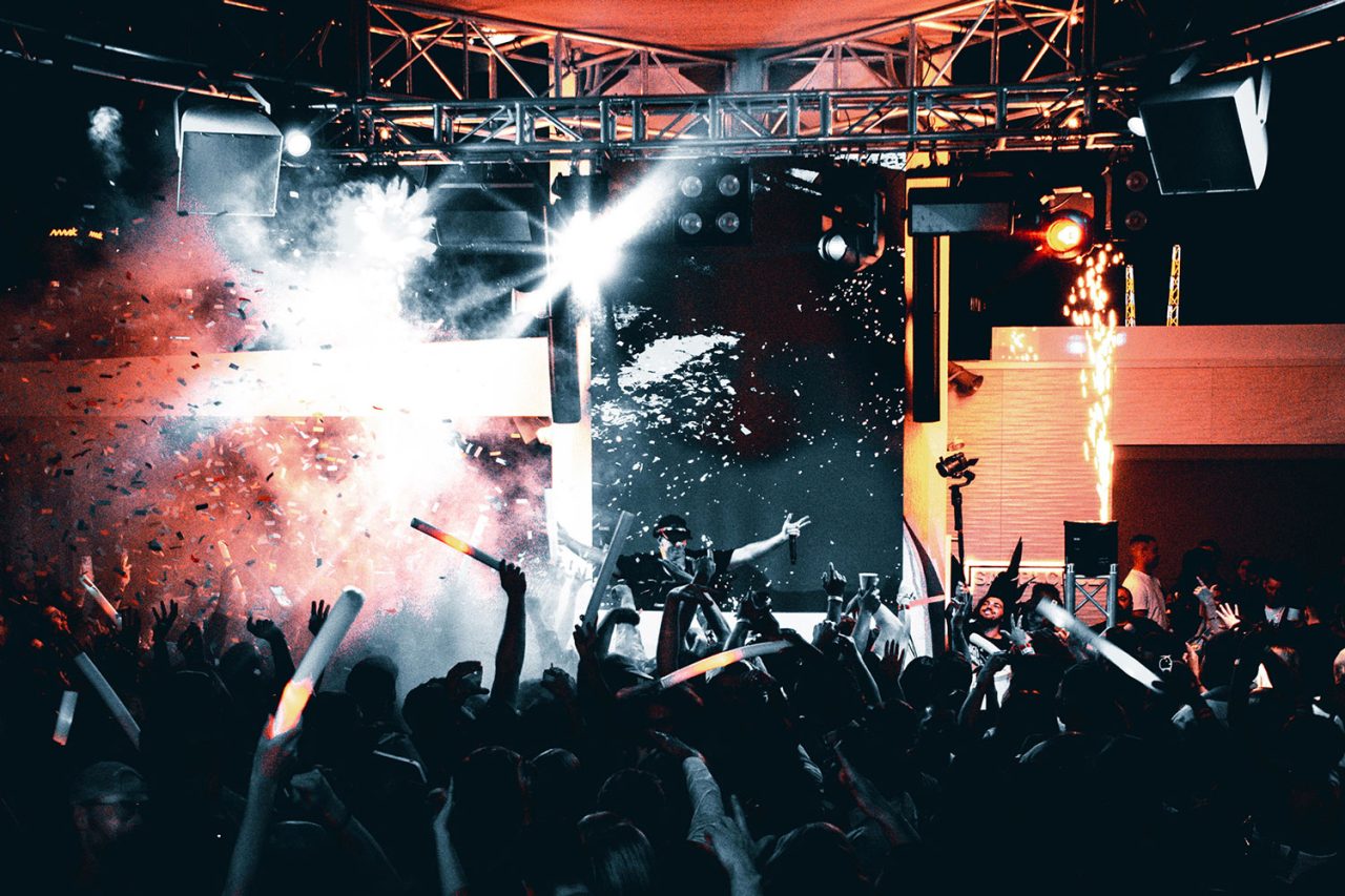 Crowd beneath stage lighting, haze and confetti at Cali Beach's birthday party.