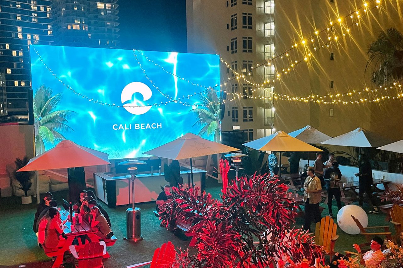 Blue Cali Beach branding on an outdoor screen above guests at the birthday celebration.