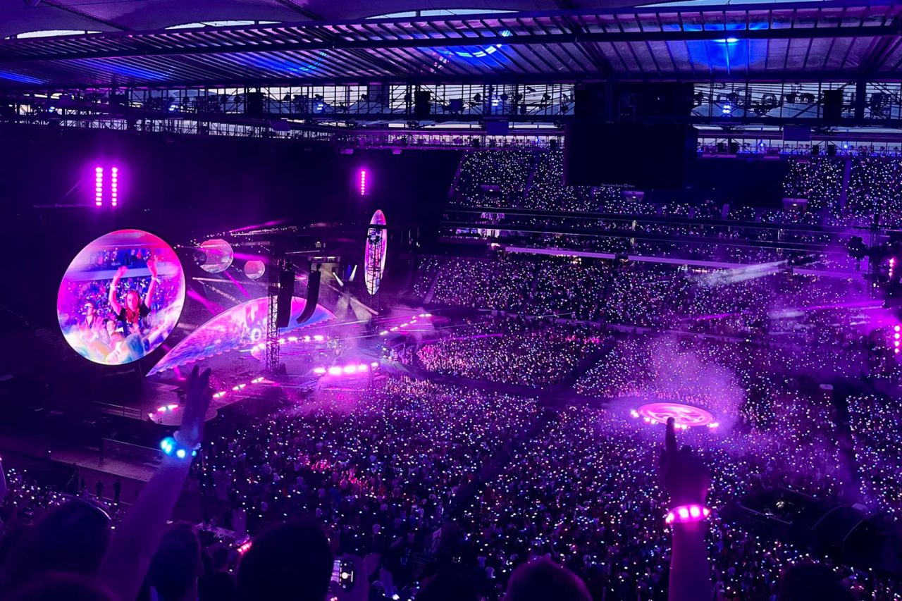 Purple light and illuminated spheres over a packed stadium on the Coldplay tour.