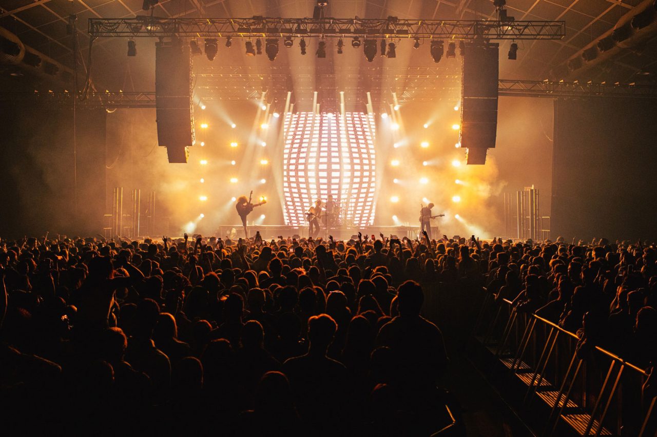 Crowd facing a gold-lit stage and vertical lighting arrays at a Spacey Jane show.